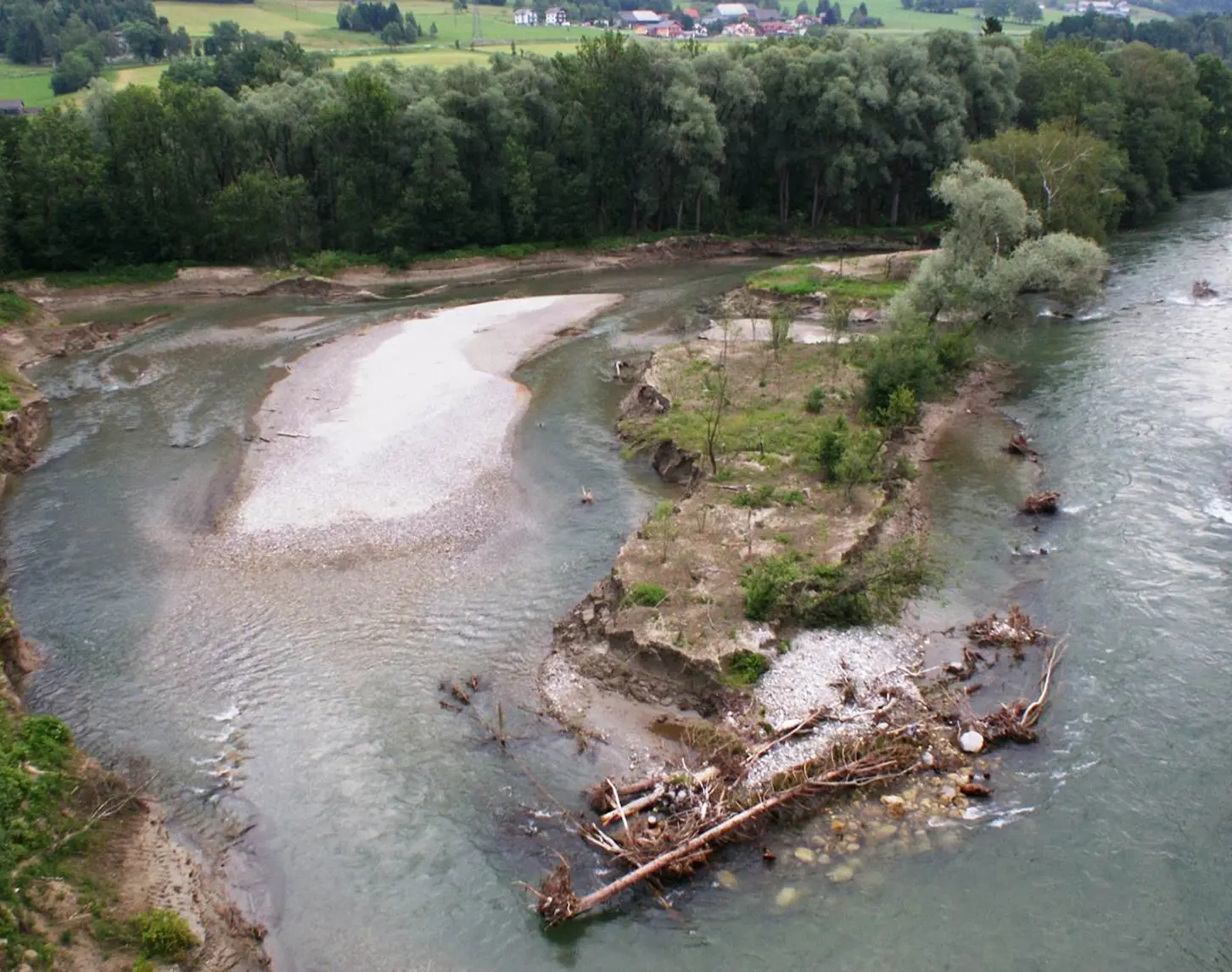 Blick auf einen Fluss mit sandigen und bewachsenen Inseln in der Mitte, umgeben von dichtem Wald. Die Strömung formt eine S-Kurve um die Inseln, während Bäume am Ufer teilweise ins Wasser ragen.